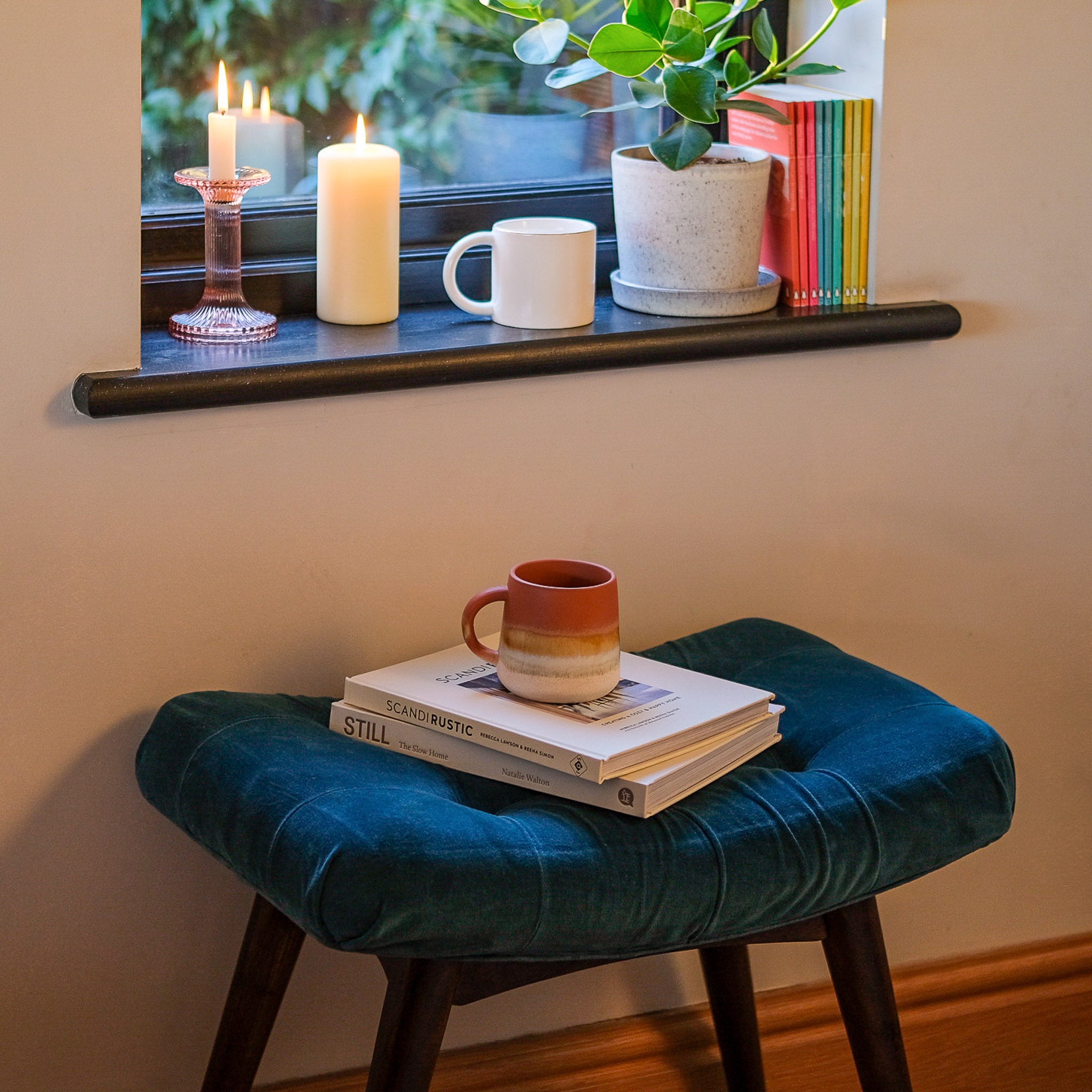 Upholstered blue velvet bench by a window, with a stylish mug and books on top.
