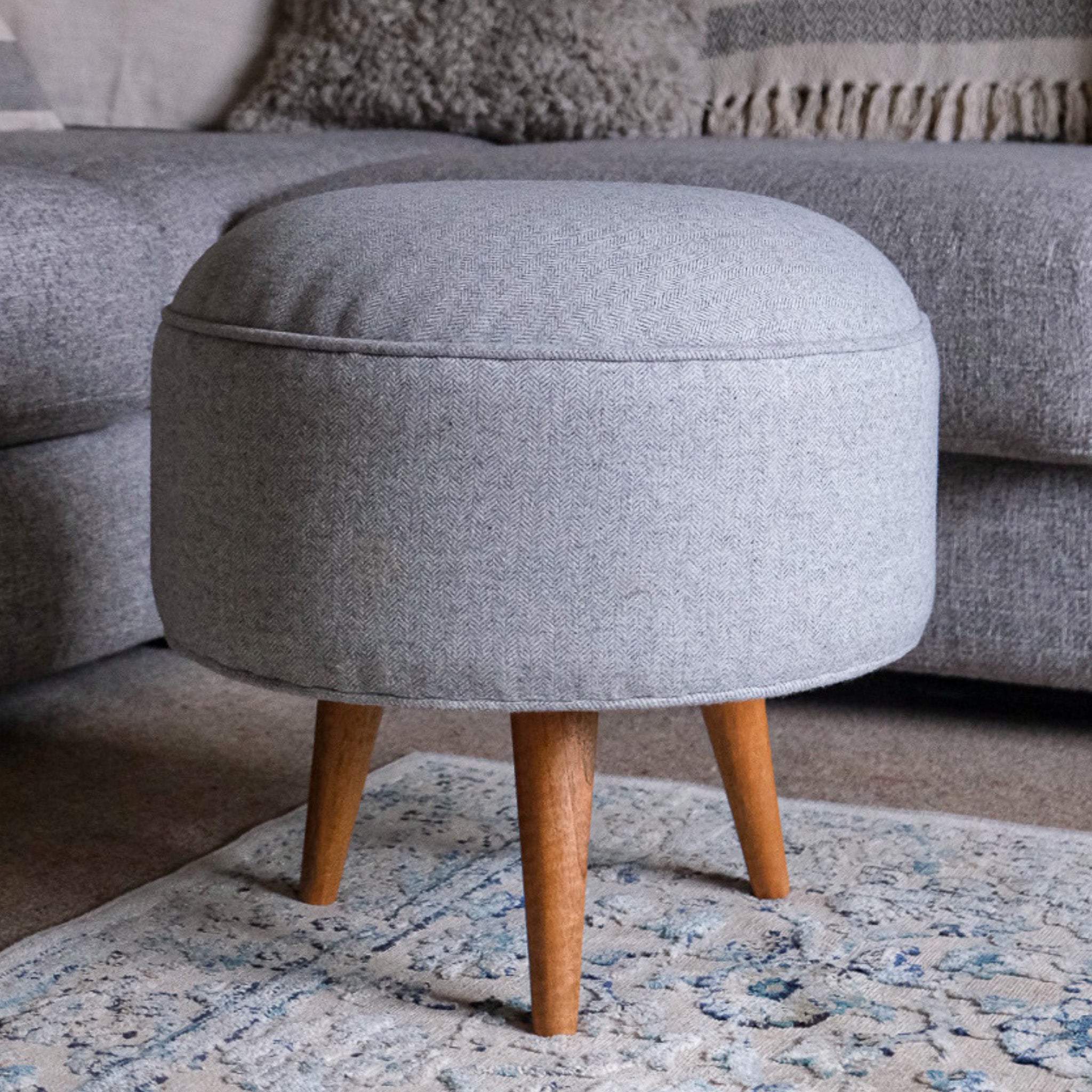 Round footstool upholstered in grey tweed in a neutral living room.