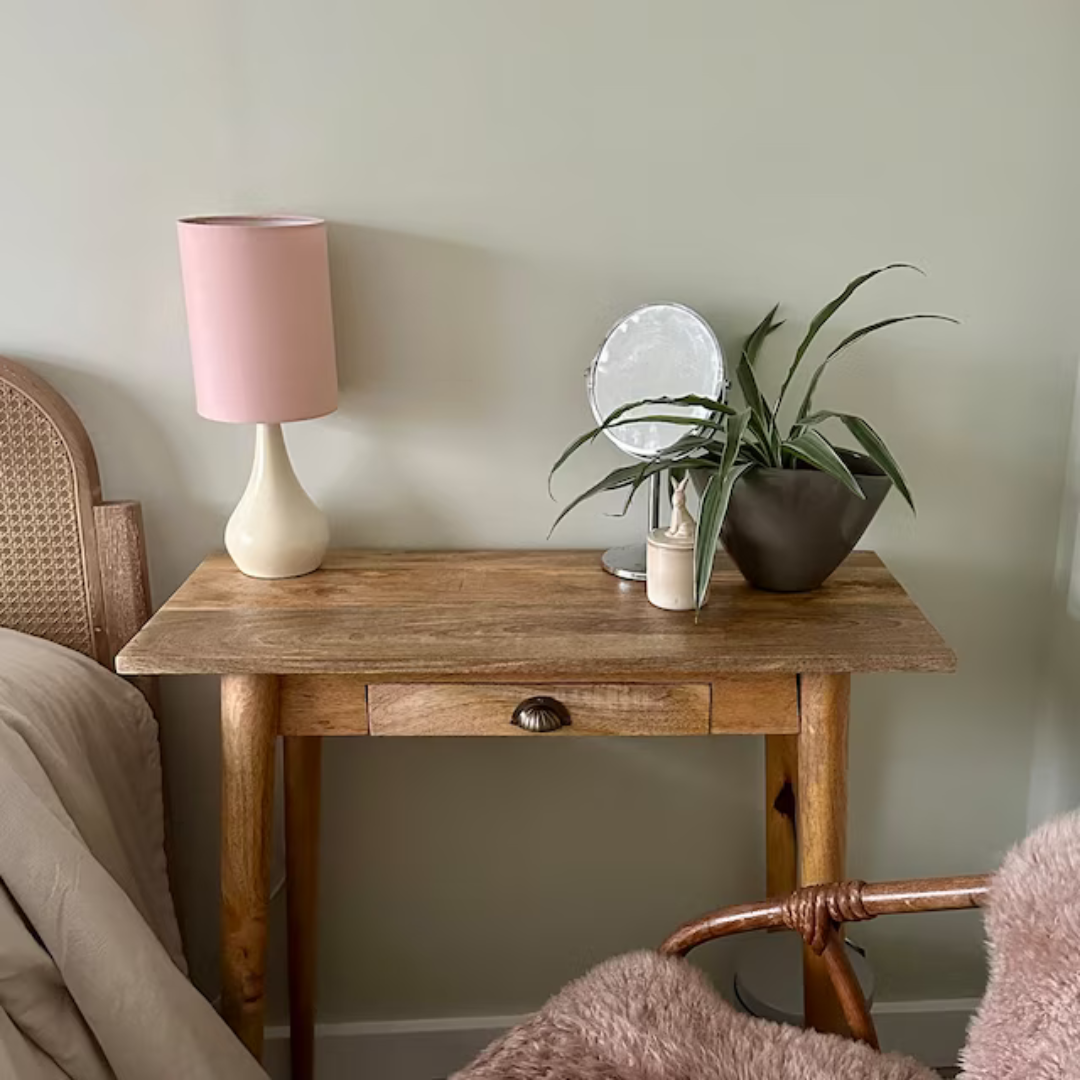 A desk styled as a bedside table in a natural wood stain.