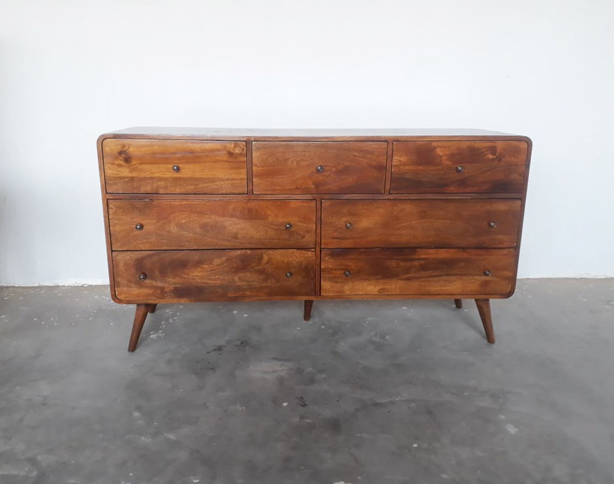 Wooden dresser with multiple drawers on a gray floor and white wall background