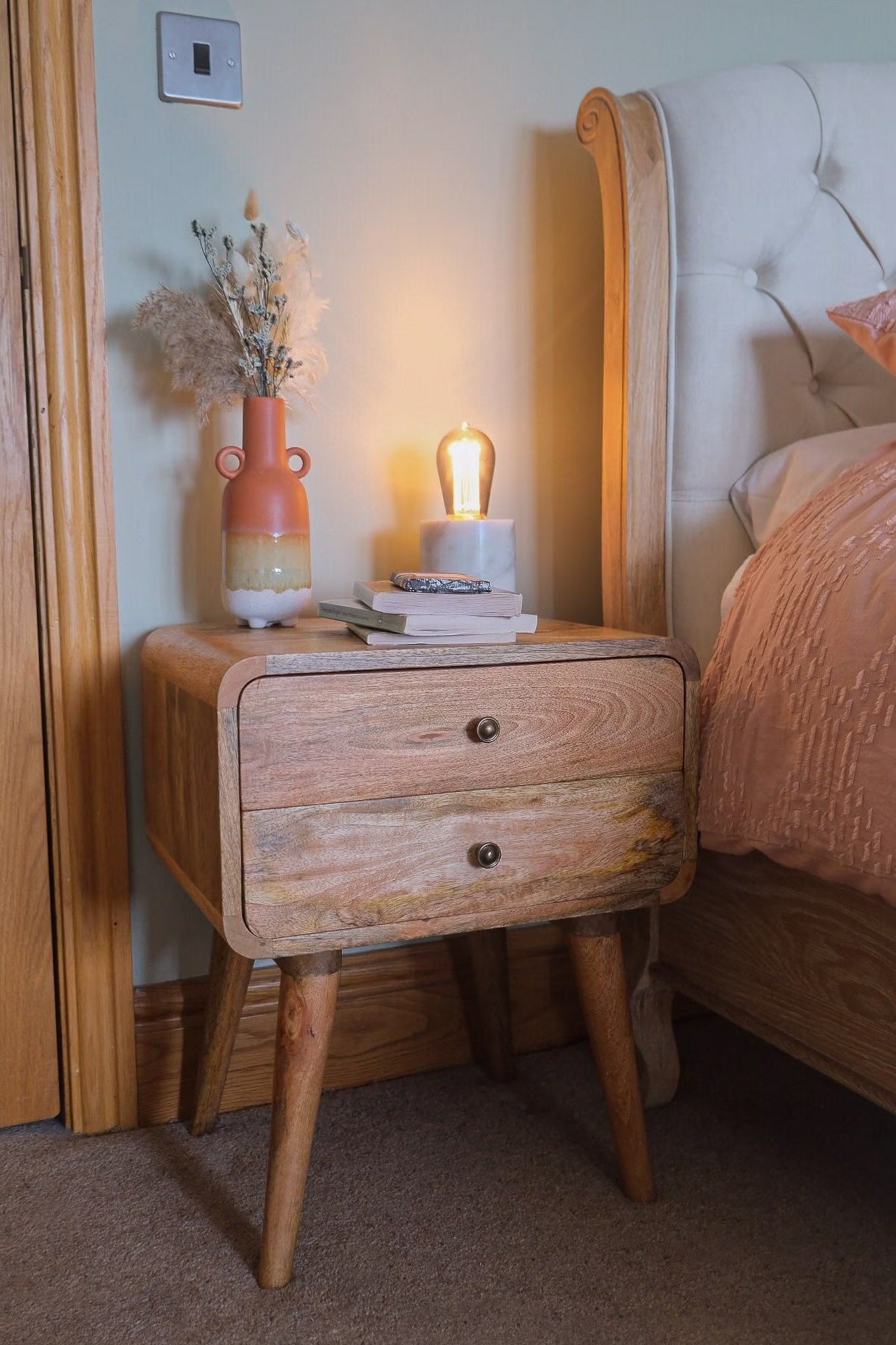 A stylish bedroom featuring a light brown mango wood nightstand.
