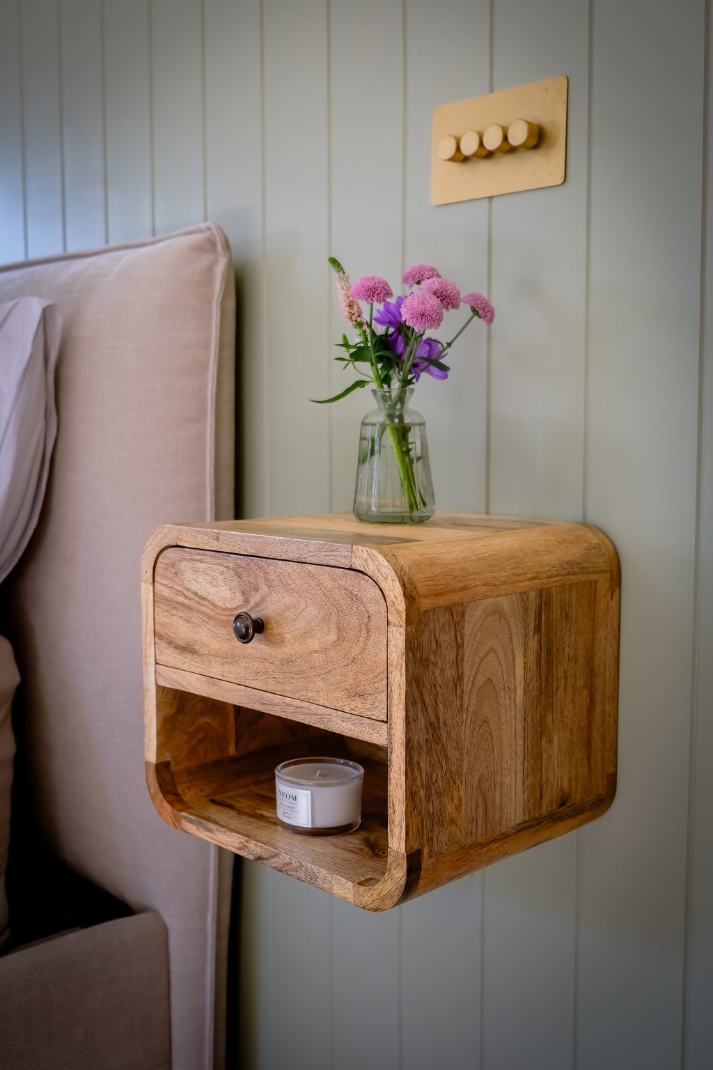 Wooden nightstand with a drawer and shelf against a light-colored wall.