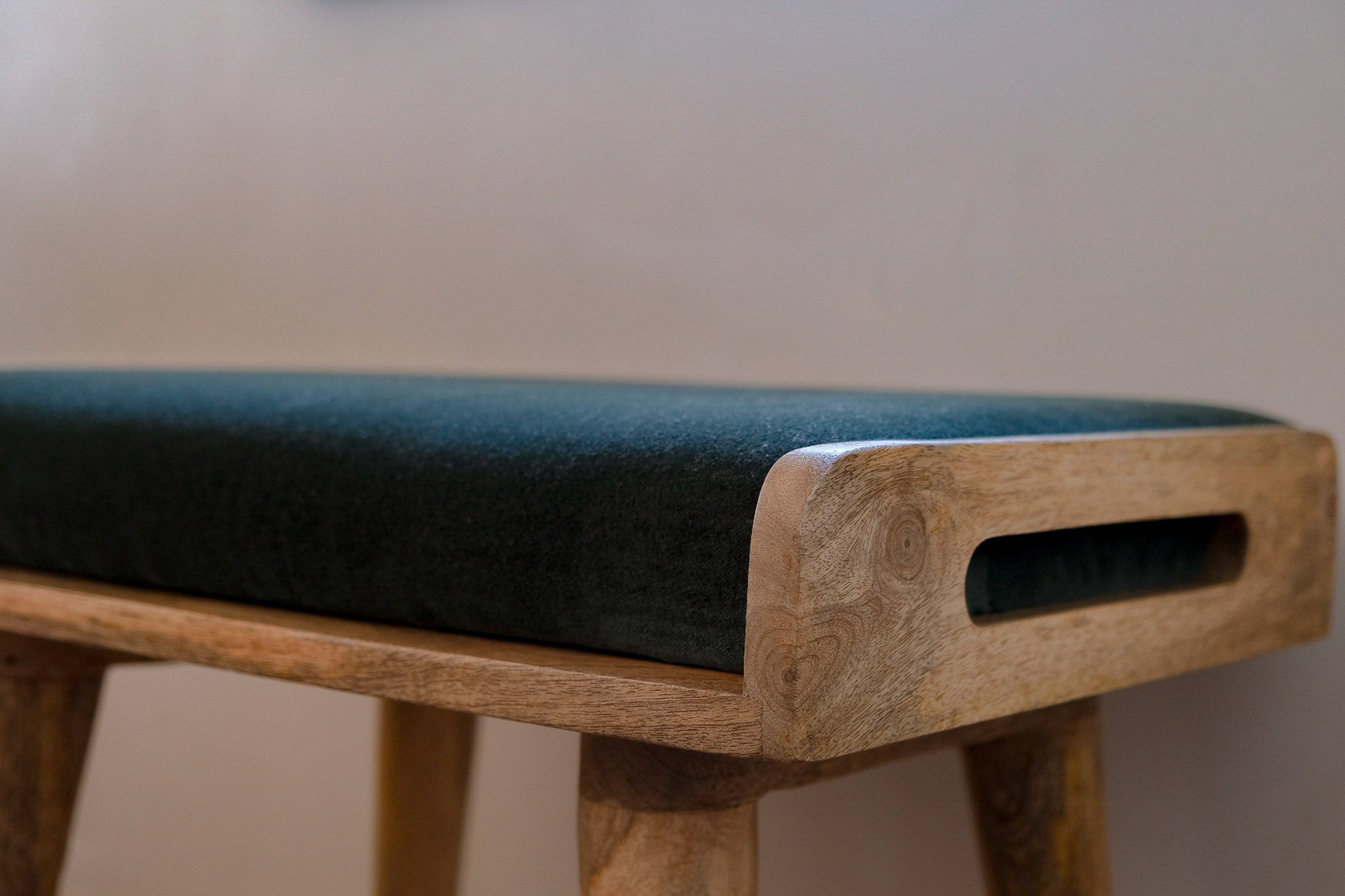 Close up shot of bench made from solid light brow wood, with a green velvet seating pad.