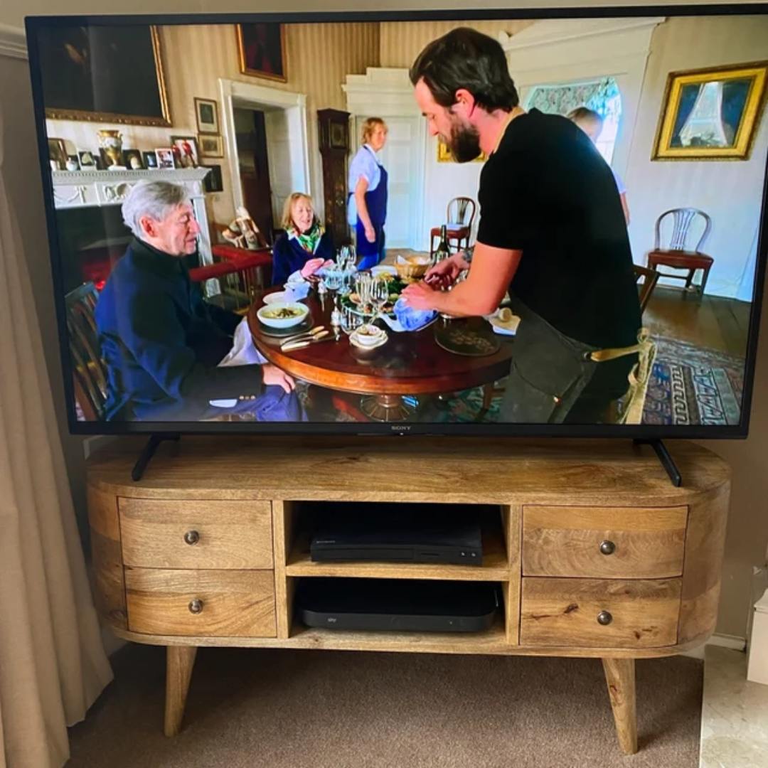 Living room showing a large TV on a solid wood media unit made from mango wood, in a light brown finish.