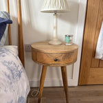 Wooden side table with a lamp and candle next to a bed