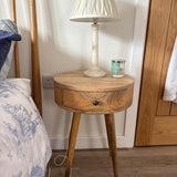 Wooden side table with a lamp and candle next to a bed