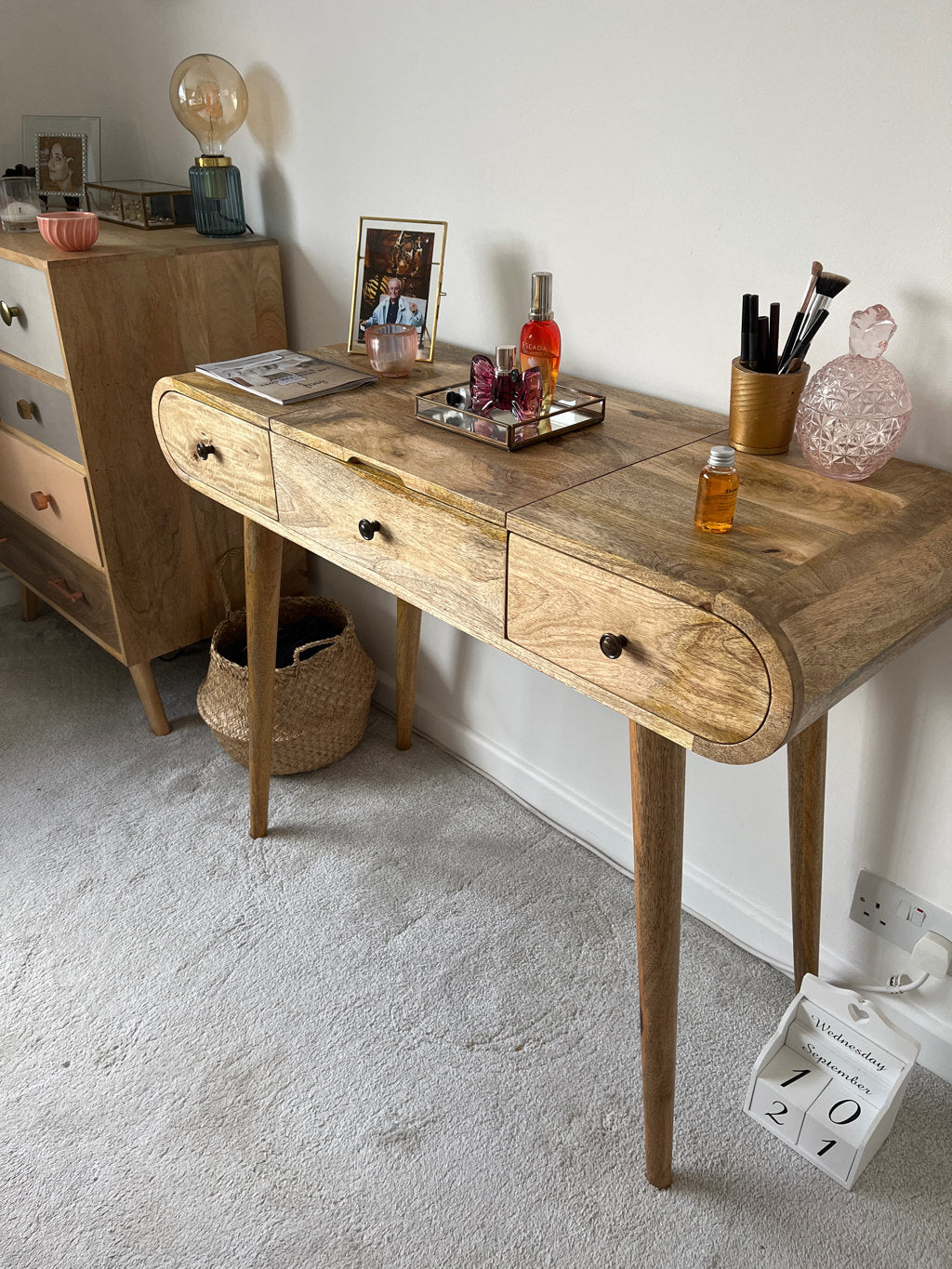 A bedroom featuring a curved dressing table made from mango wood, in a light brown stain.