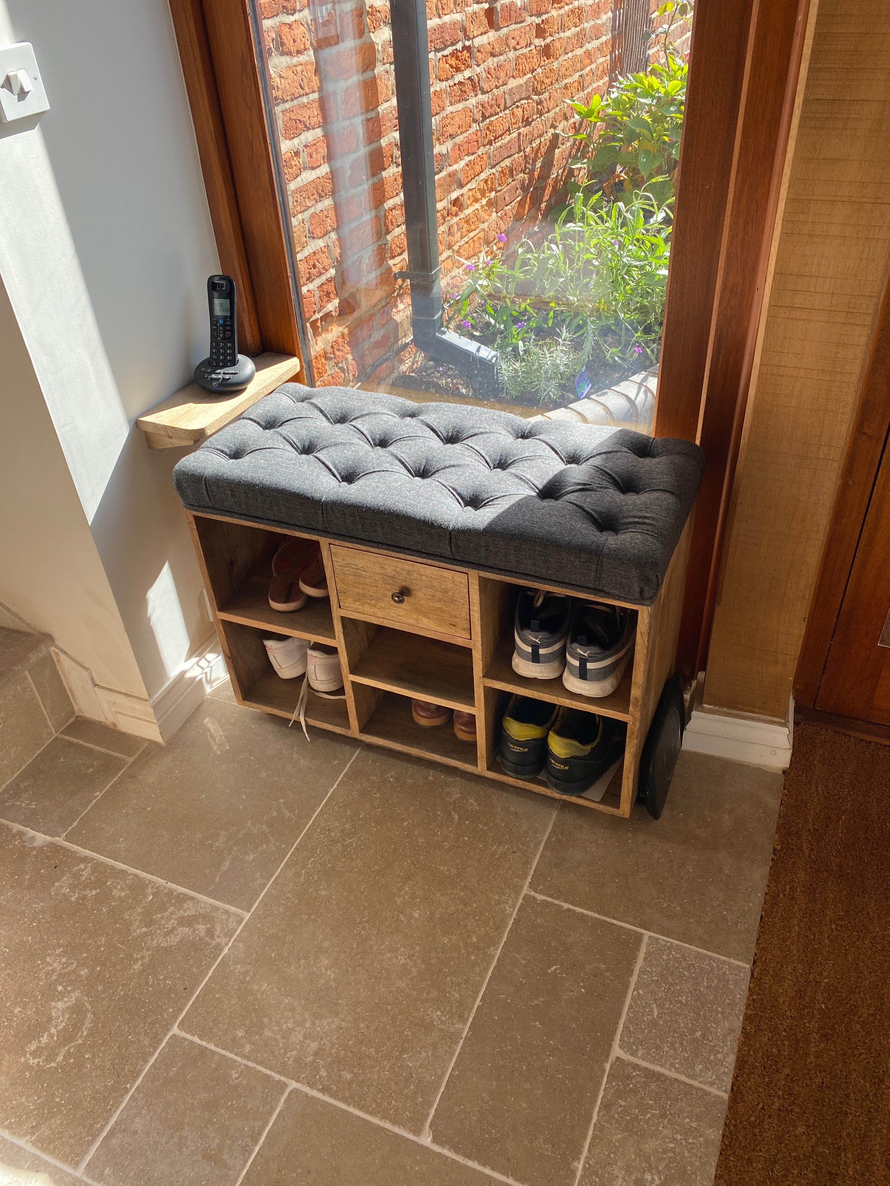 Neutrual entryway with wooden shoe storage bench, with a black tweed seating pad.