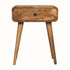 A medium-sized bedside table made of solid mango wood with a natural finish, featuring a single drawer and four long tapered legs with brass hardware.