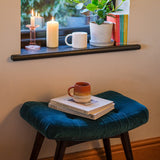 Upholstered blue velvet bench by a window, with a stylish mug and books on top. 