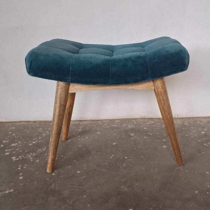 Teal upholstered stool with wooden legs on a concrete floor.