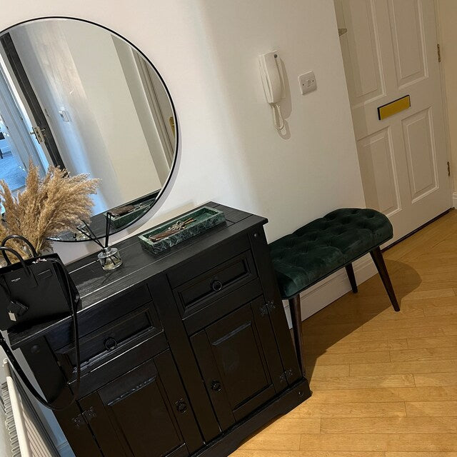 Dresser with round mirror, black bag, and green bench in a room.