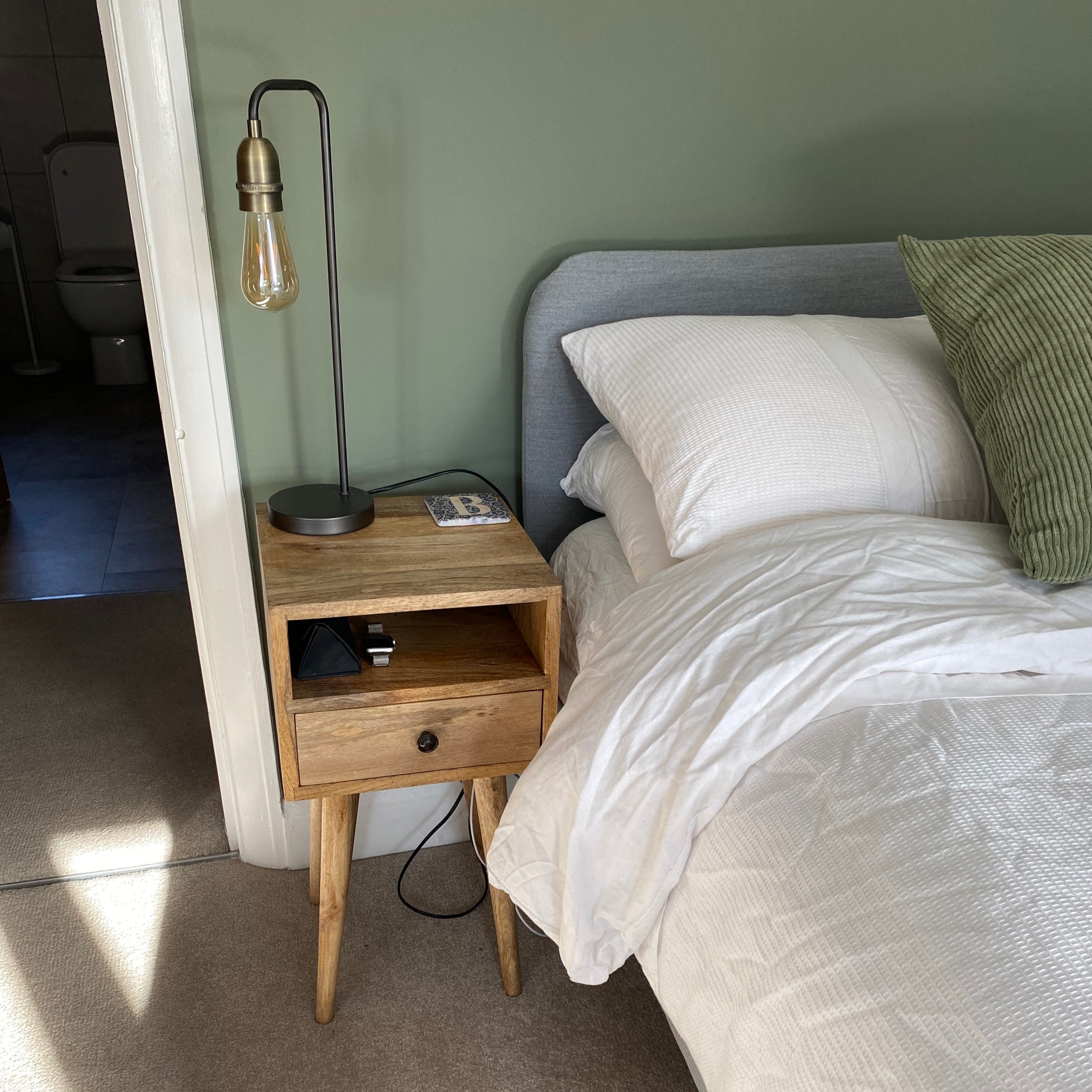 Bedroom with small mango wood nightstand, lamp, and bed with pillows.
