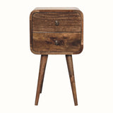 A small bedside table with four legs, made of mango wood with a grey wash finish, featuring two drawers with brass knobs.