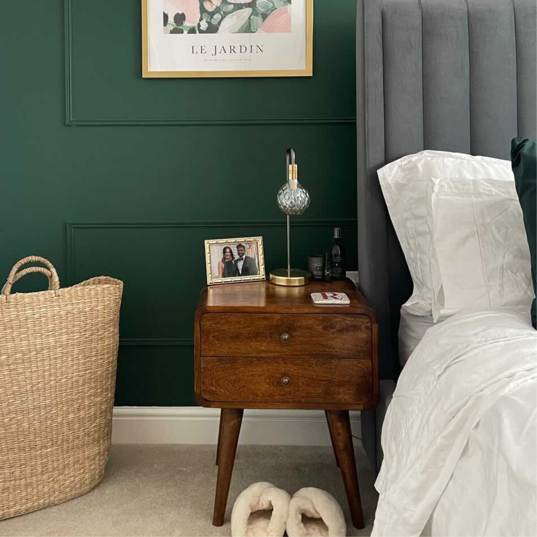 Bedroom with wooden nightstand, lamp, and framed picture against a green wall.