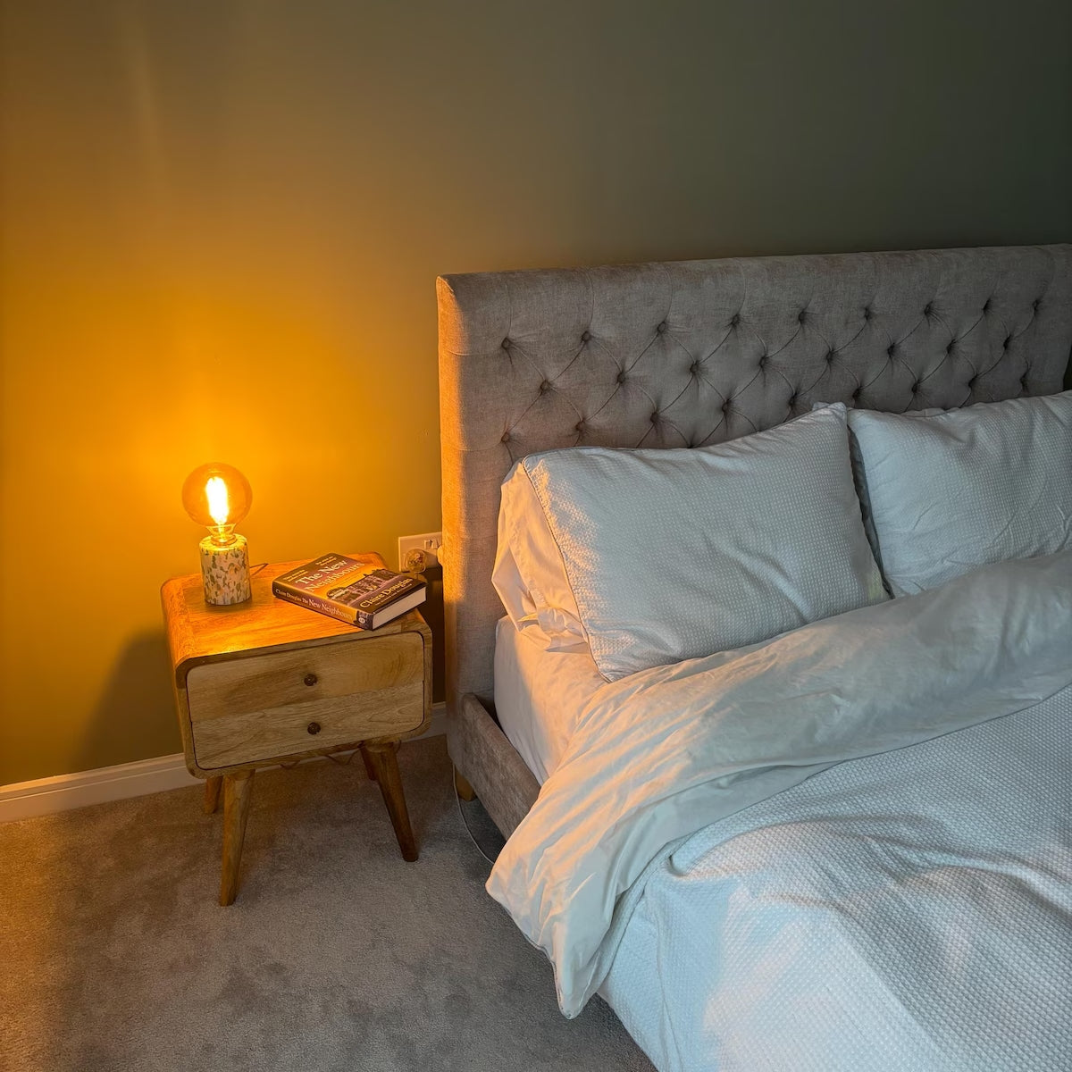 Bedroom with a tufted headboard, nightstand with lamp, and books.