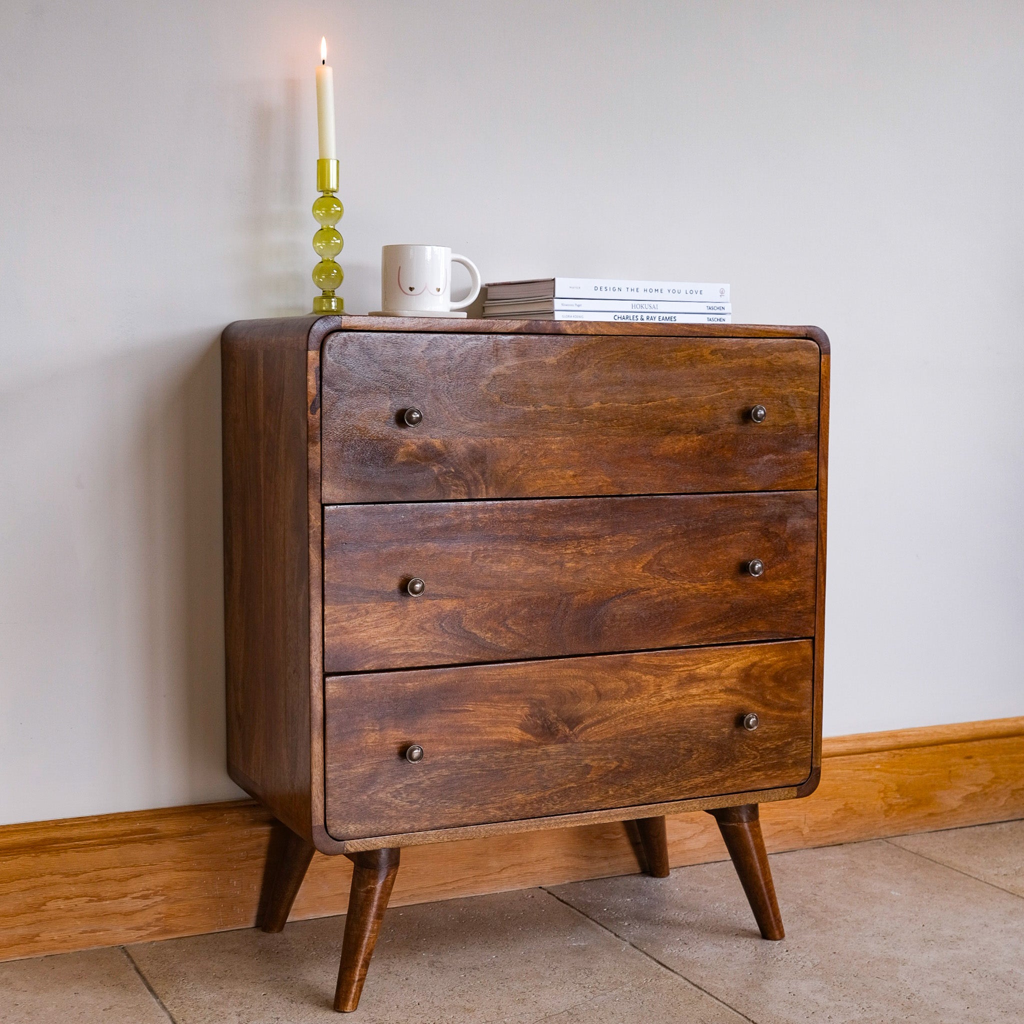 Curved chest of drawers in a neutral room with home decor on top. 