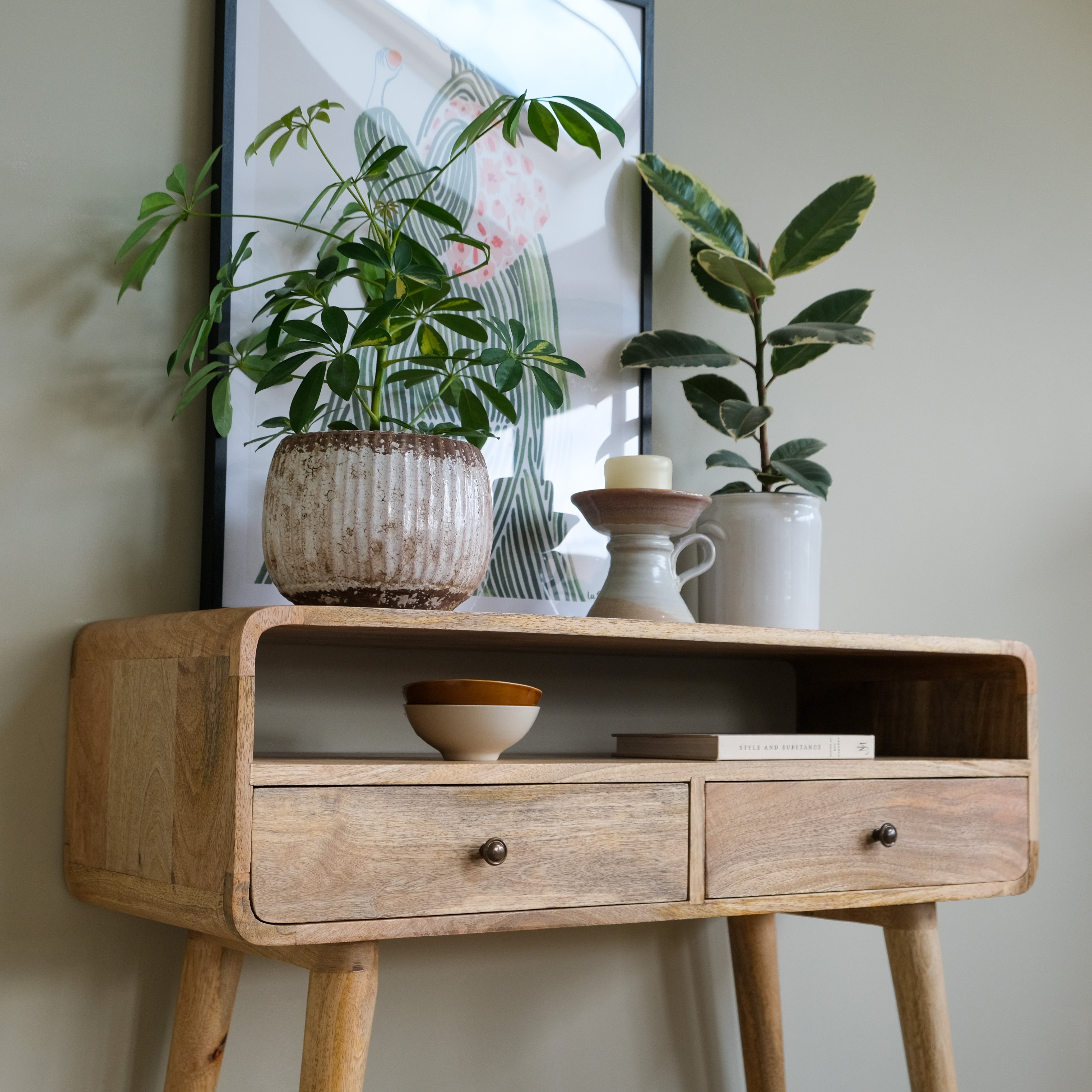 Mango wood console table with decorative items and plants against a neutral wall.