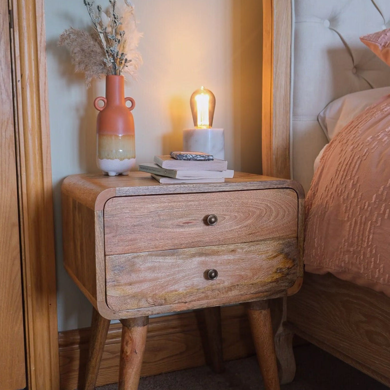 A stylish bedroom featuring a light brown mango wood nightstand.  