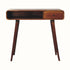 A chestnut-finished mango wood writing desk with four legs, one drawer with a brass knob, and an open slot shelf.