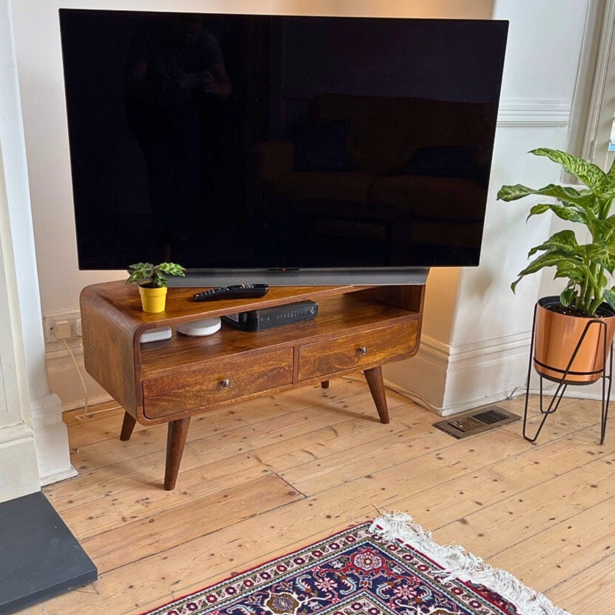 A stylish living room, featuring a large TV that is styled on top of a dark wood media unit, with a curved body and storage.
