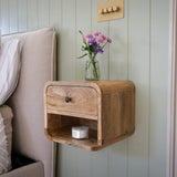 Wooden nightstand with a vase of flowers on a bed in a bedroom.