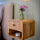 Wooden nightstand with a drawer and shelf against a light-colored wall.