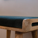 Close up shot of bench made from solid light brow wood, with a green velvet seating pad.