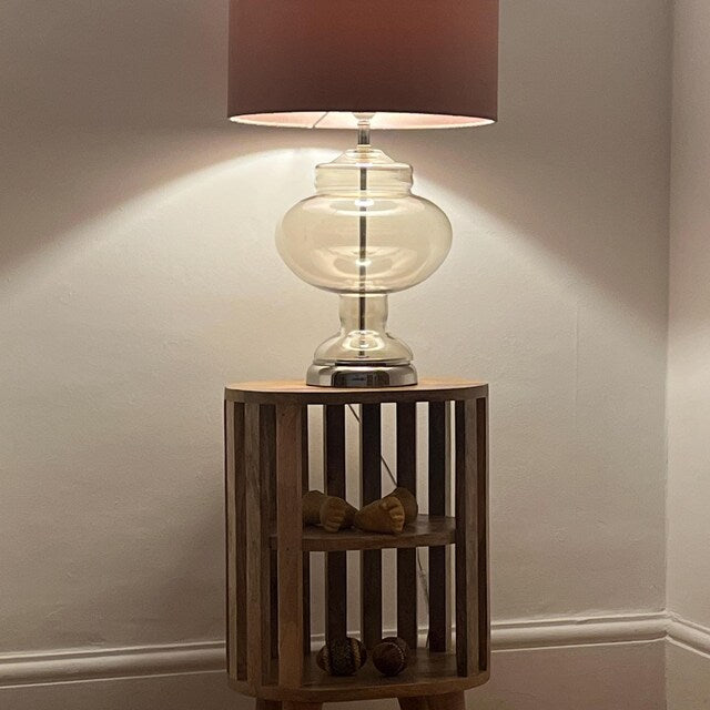 Wooden side table with a lamp and decorative items against a neutral wall.