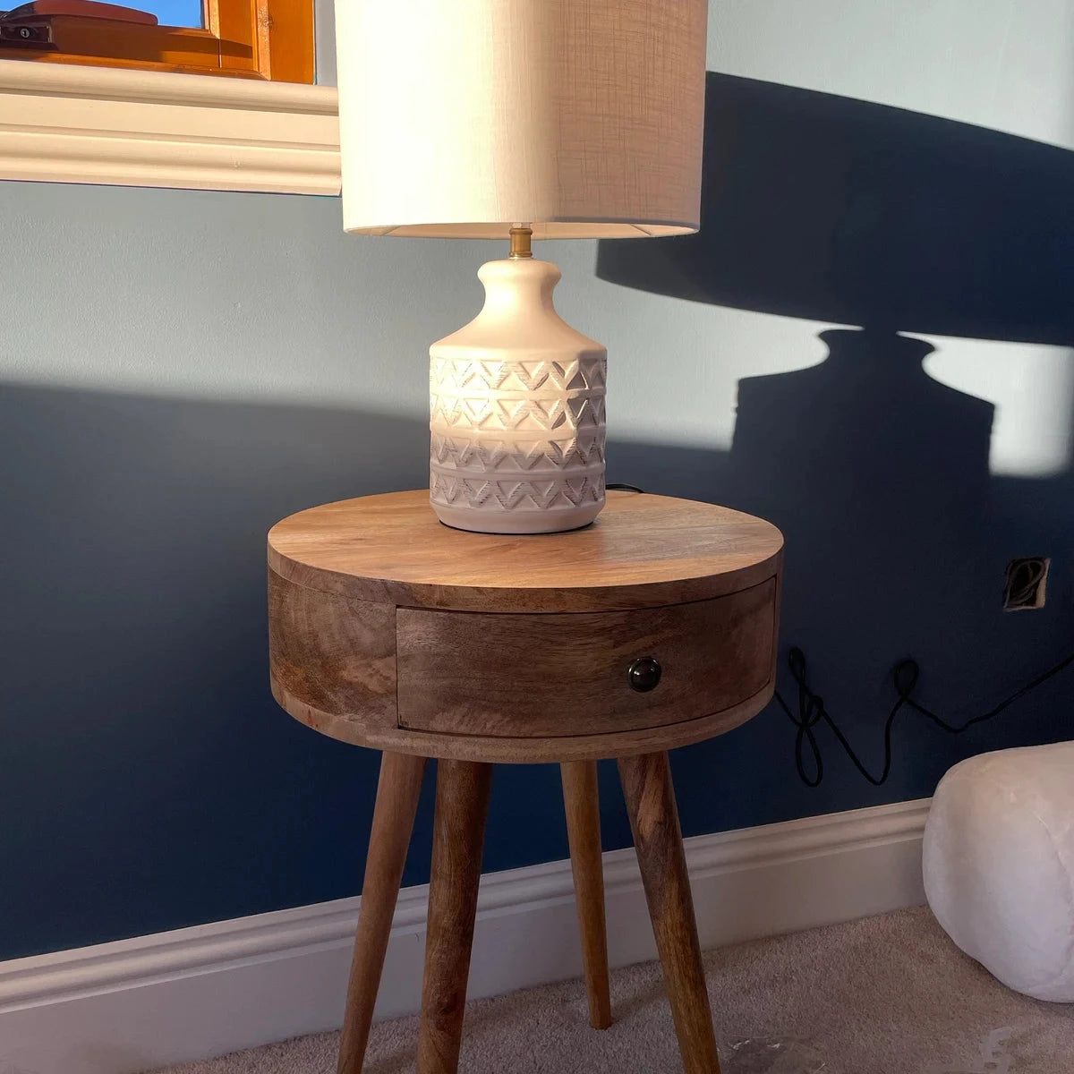 Circular mango wood side table with a lamp against a blue wall
