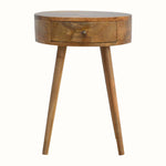 A natural finish bedside table made of mango wood, featuring a round top and a single drawer with a brass knob.