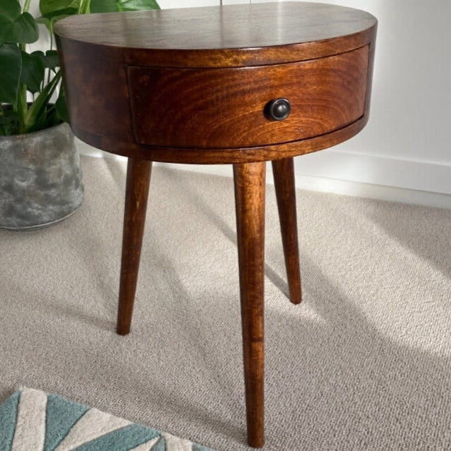 A semi circular shape bedside table made from mango wood in a dark brown finish, featuring a small drawer and single brass knob.