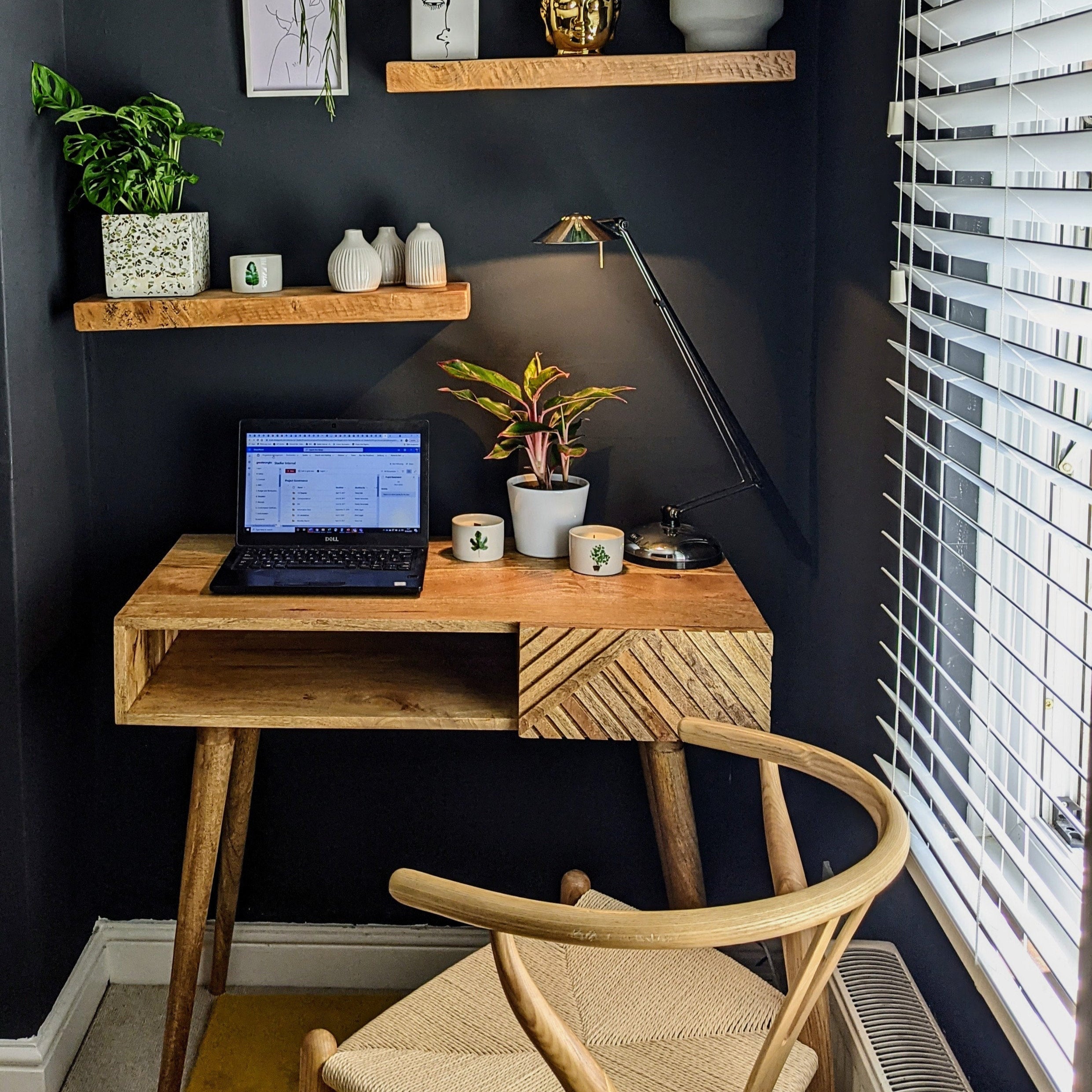 Light brown mango wood desk with laptop, chair, and decorative items against a dark wall.