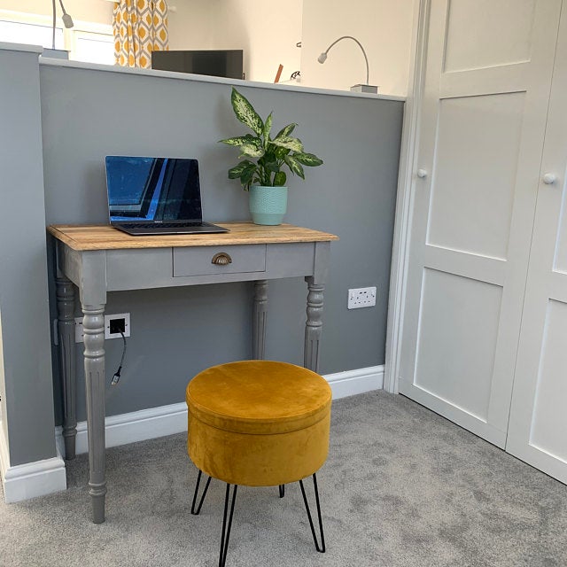 Small home office with a desk, laptop, plant, and yellow stool against a gray wall.