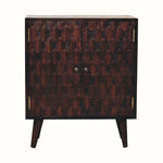 A small light walnut Marina cabinet with two carved doors featuring a pineapple pattern and brass knobs, perched on four short Nordic-style legs.