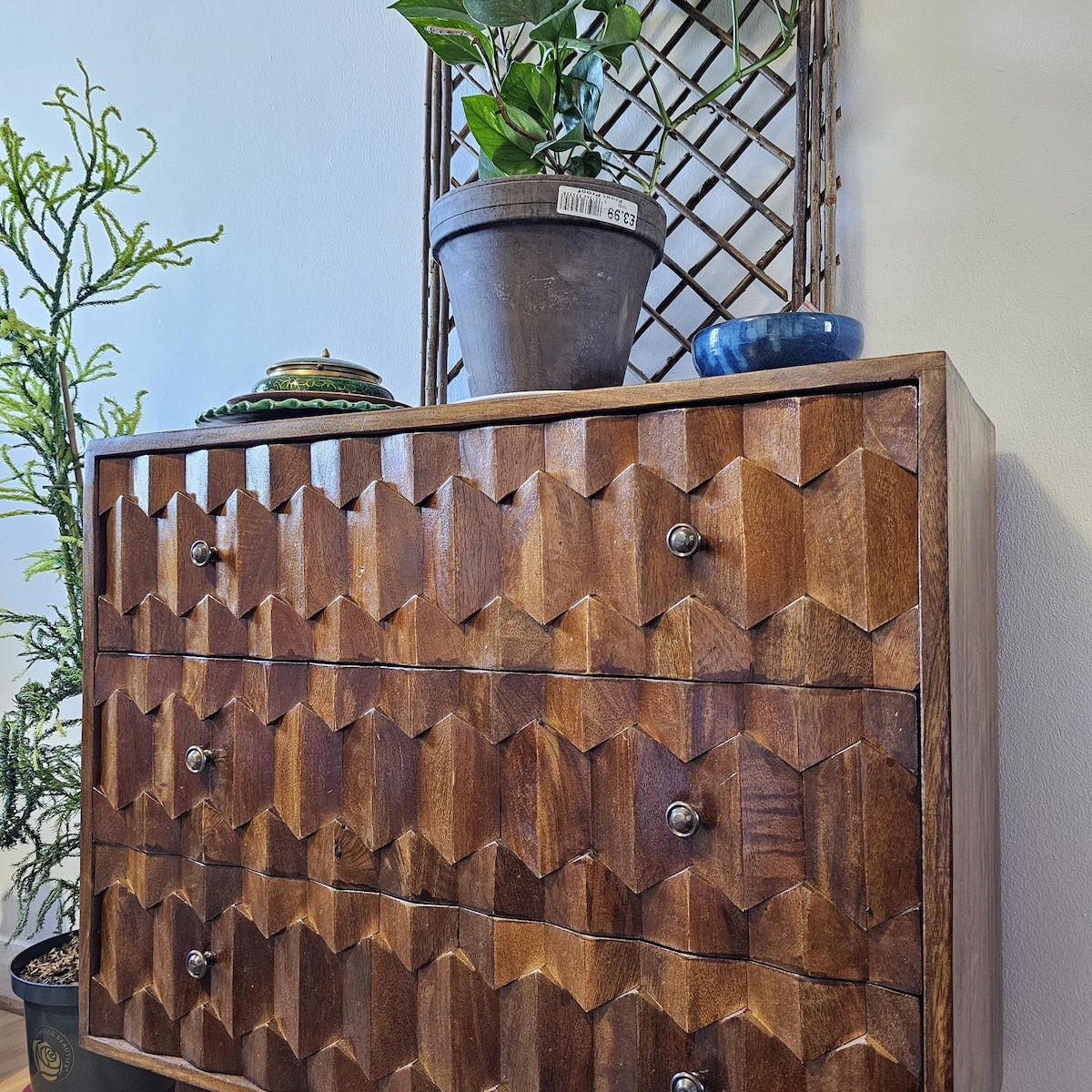 Mango wood chest of 3 drawers with geometric pattern and decorative items on top against a light blue wall.