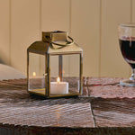 Candle lantern with a lit candle on a wooden surface next to two glasses of red wine.