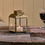 Candle lantern with a lit candle on a wooden surface next to two glasses of red wine.