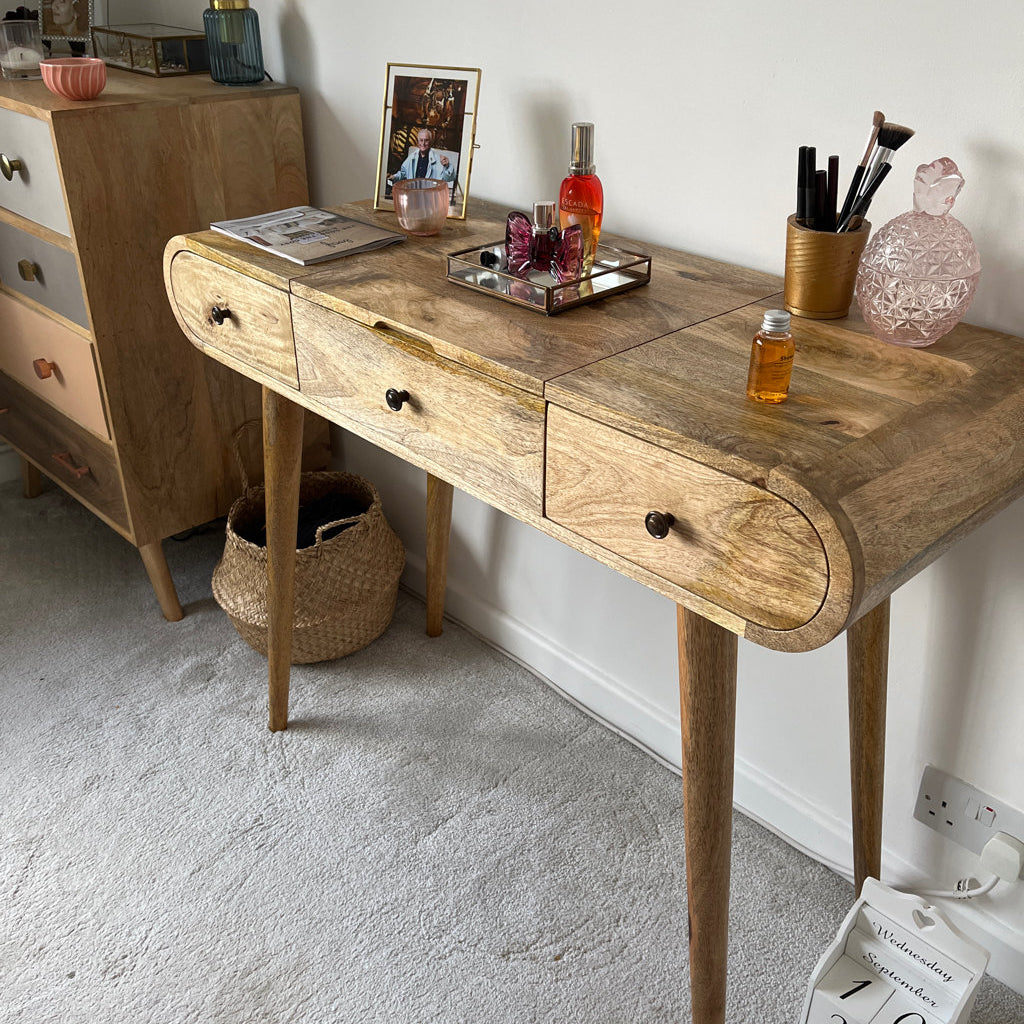 A bedroom featuring a curved dressing table made from mango wood, in a light brown stain.