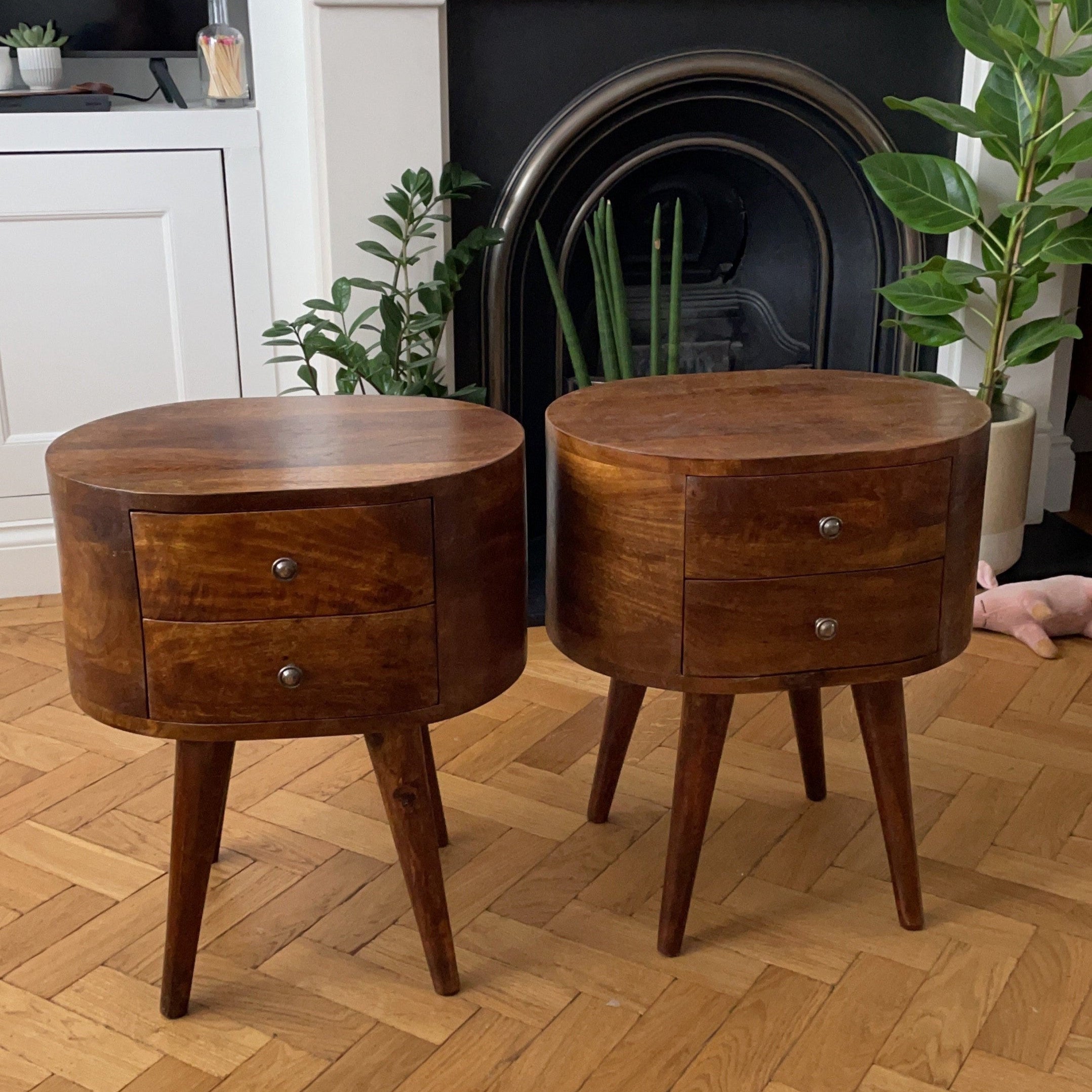 Two dark brown mango wood bedside tables with drawers on a wooden floor inside a living room.