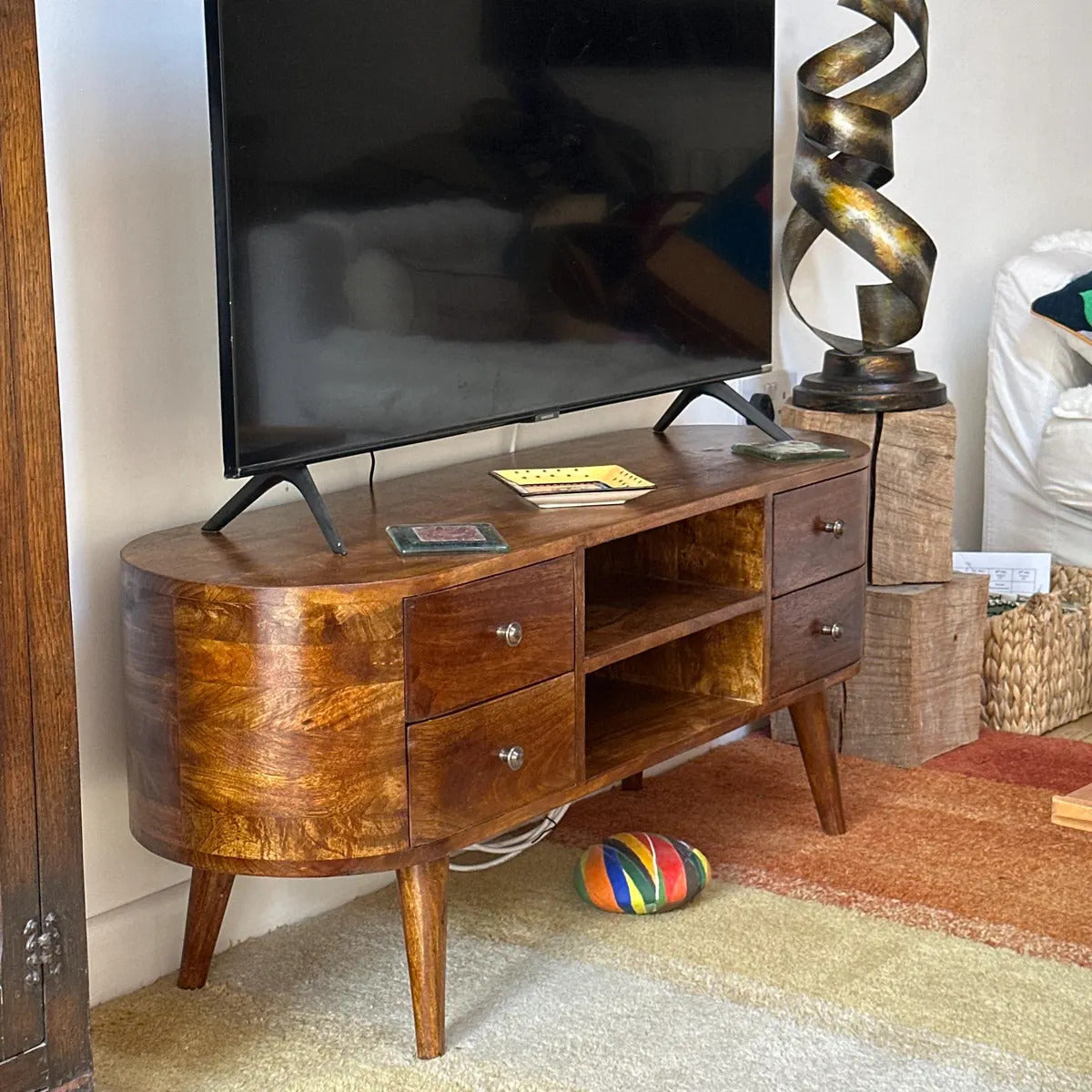 Dark brown mango wood TV stand with a television on top in a living room setting.