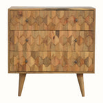 A medium-sized chest of drawers with a natural finish, featuring a hand-carved pineapple pattern on the front and brass knobs. It is on four short Nordic-style legs.