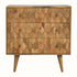 A medium-sized chest of drawers with a natural finish, featuring a hand-carved pineapple pattern on the front and brass knobs. It is on four short Nordic-style legs.