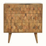 A medium-sized chest of drawers with a natural finish, featuring a hand-carved pineapple pattern on the front and brass knobs. It is on four short Nordic-style legs.