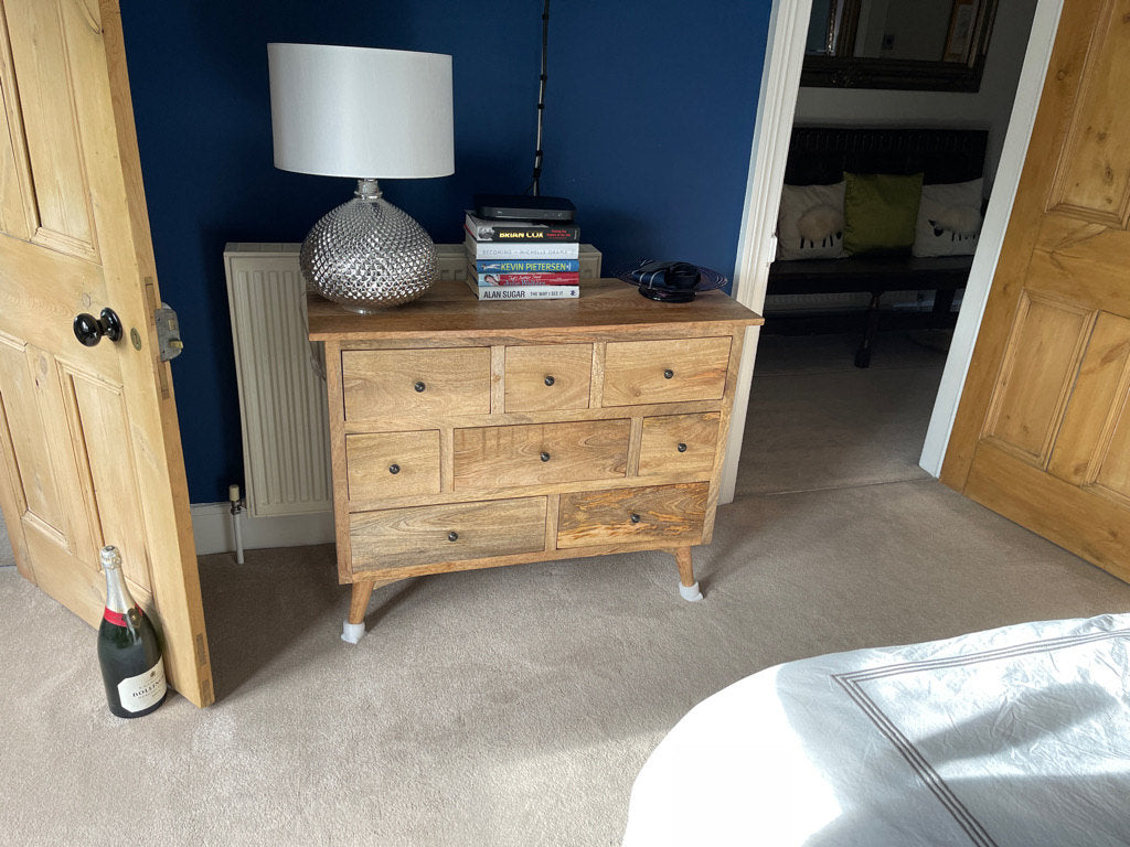 Mango wood chest of drawers in a light brown finish, with a lamp and books against a blue wall in a room.