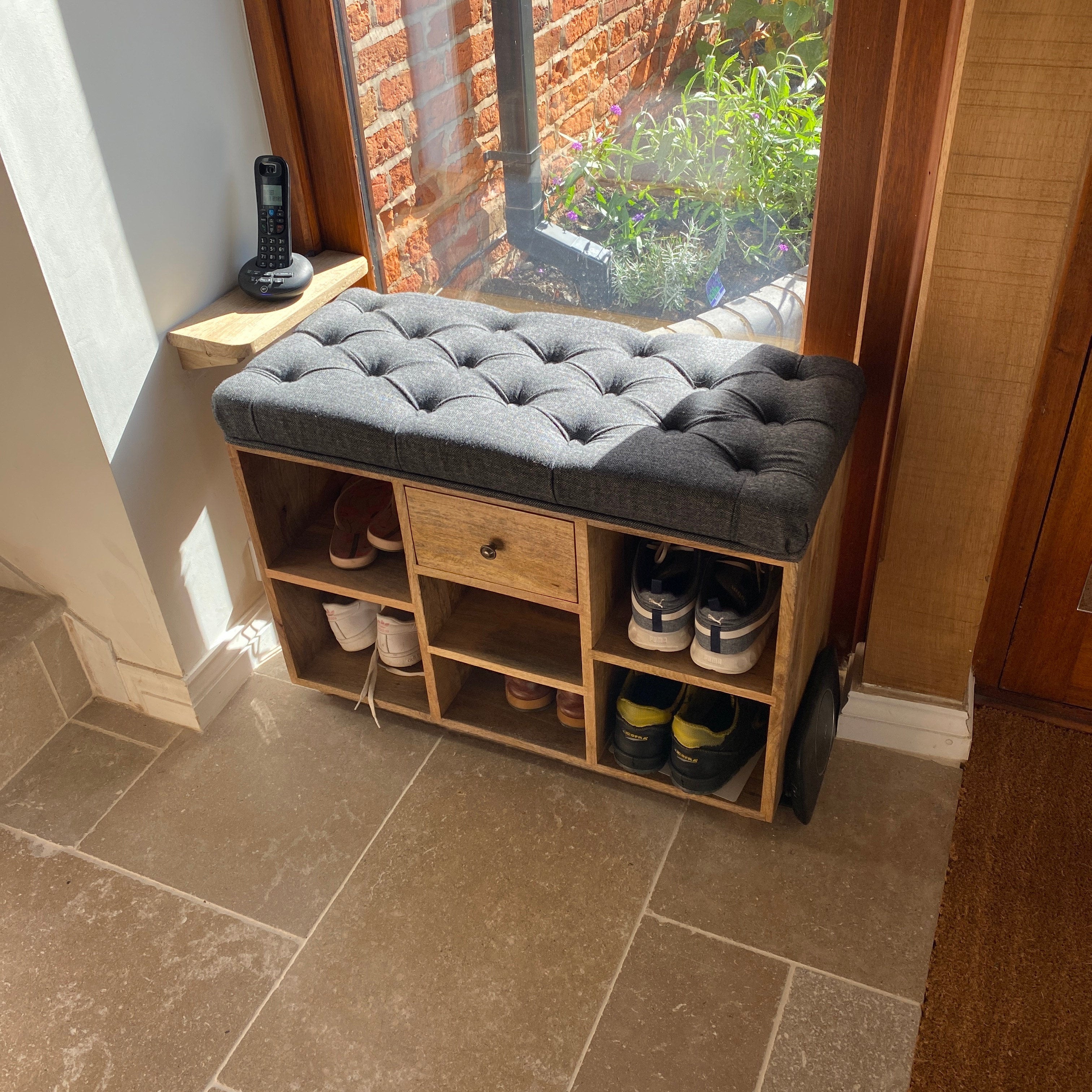 Neutrual entryway with wooden shoe storage bench, with a black tweed seating pad.