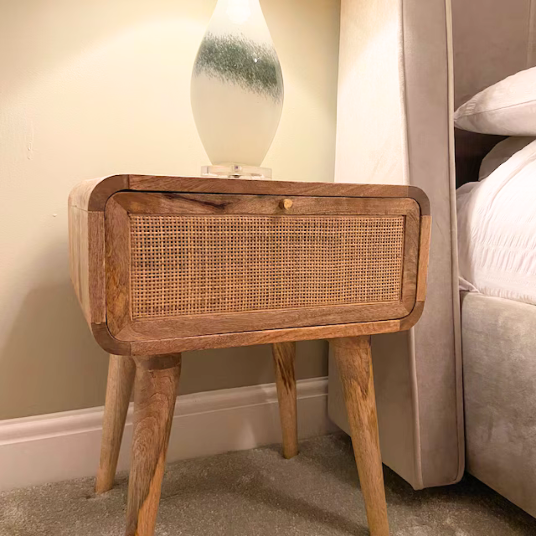 A modern Scandinavian style bedside table featuring a curved-shaped body that is made from mango wood, with a woven drawer front in a natural finish.