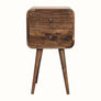 A small bedside table with four legs, made of mango wood with a grey wash finish, featuring two drawers with brass knobs.