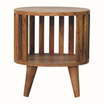 A round bedside table made of natural wood with a slatted design and a single shelf underneath. The table has a compact and sturdy structure with visible wood grain.