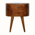 A round chestnut-colored bedside table made of mango wood with two drawers and four tapered legs, featuring brass knobs.